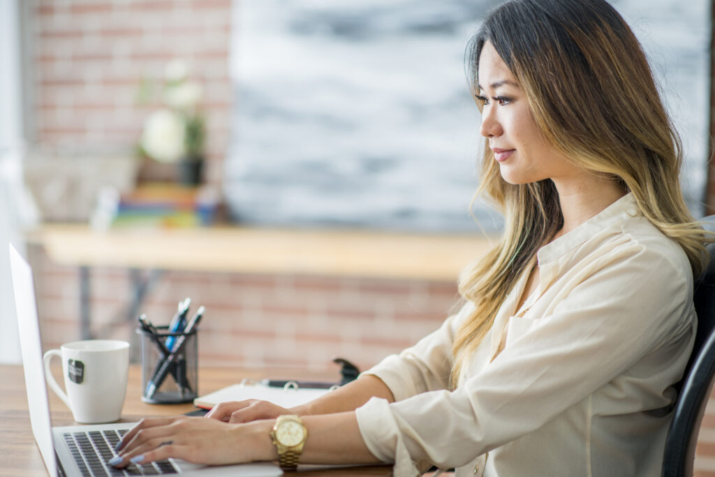 A woman using a laptop, smiling quietly to herself, perhaps because she uses Office to manage additional childcare subsidy ACCS