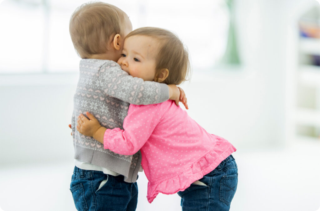 Two young toddlers hugging, perhaps mimicking behaviour modeled by educators, evidence of effective leadership in childcare