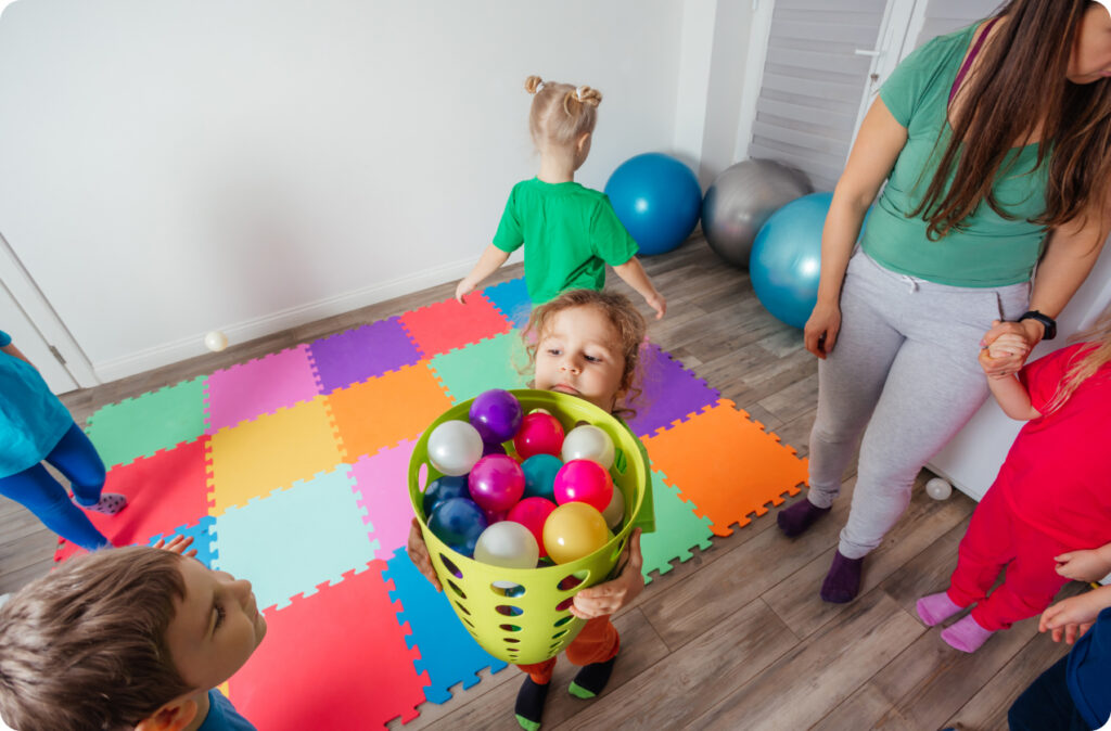 A young girl at a childcare struggling to carry a basket of balls