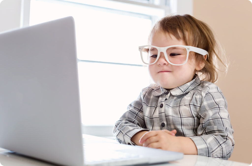 A young child wearing white-framed eyeglasses, scrutinising a computer screen, as if reviewing a Child Care Management System (CCMS) application