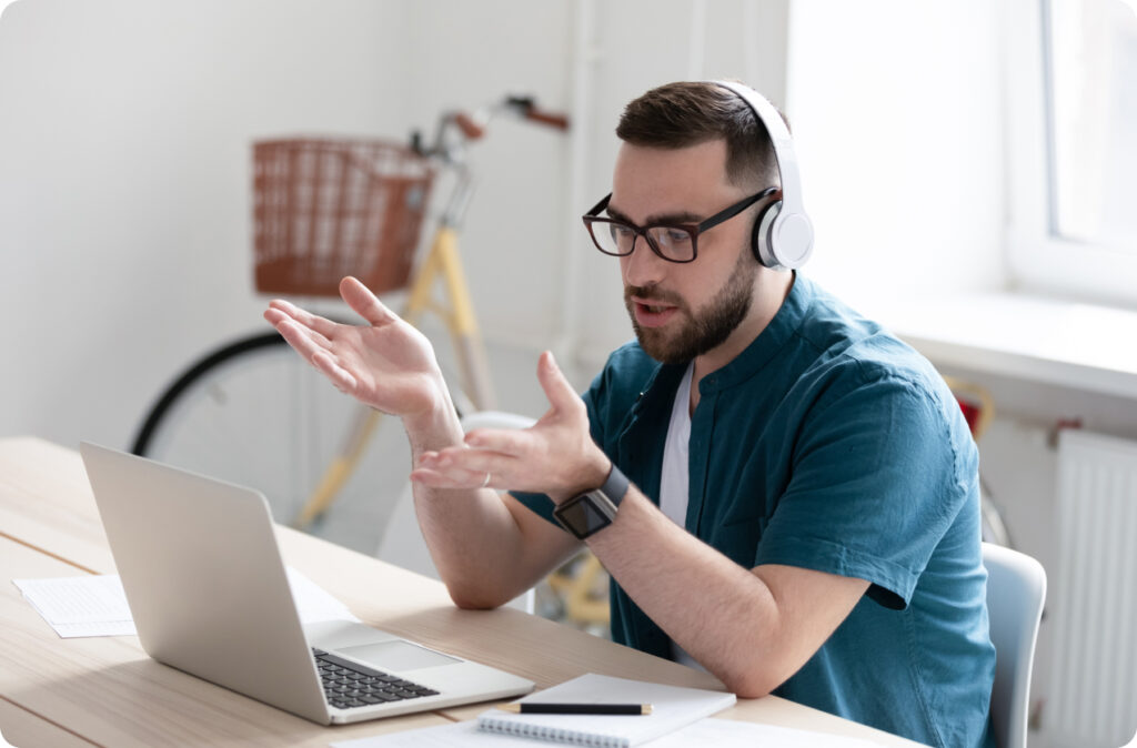 A man gesturing at a laptop screen while wearing headphones, expressing frustration that his all-in-one childcare solution isn't actually an all-in-one platform