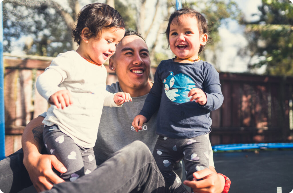 A father playing with his two young children on a trampoline