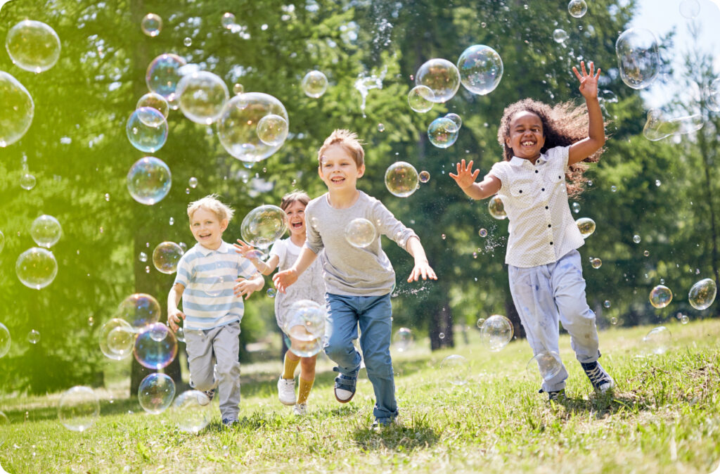 Several young children running outside, chasing bubbles